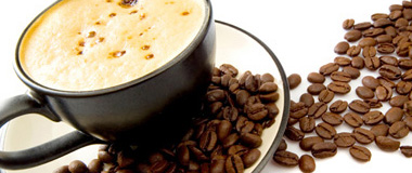 Pohled na šálek kafe, který je položený na stole s rozsypanými zrnky kávy